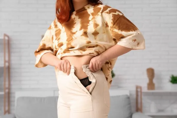 Image of woman trying to do her trousers up after pregnancy weight gain Ilford