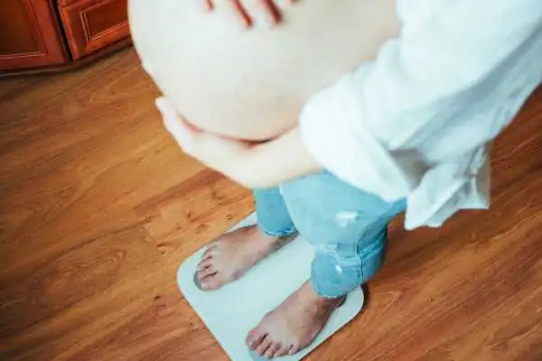 Image of woman weighing herself and experiencing weight gain through pregnancy Ilford
